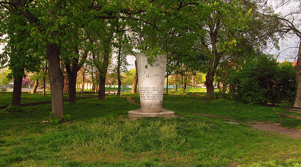 Pomník stojí na hrotu ostrova mezi náhonem a řekou, poblíž železniční vlečky.