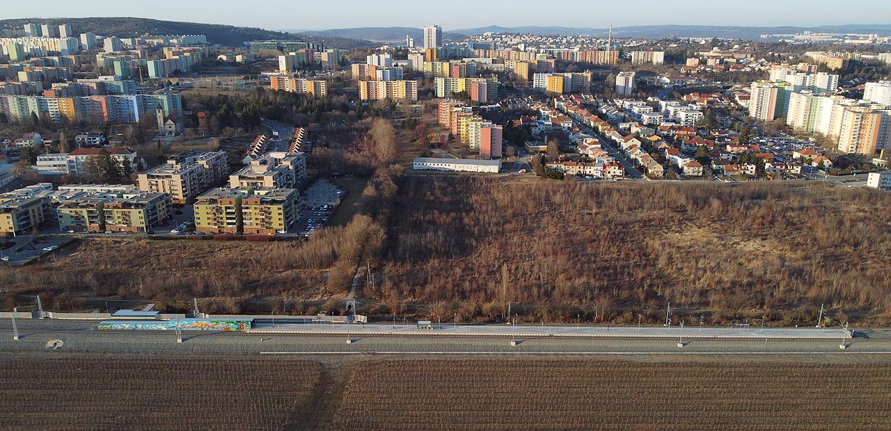 Celkový pohled na zastávku Brno-Starý Lískovec z jihu. Za pustým „rozvojovým územím", na kterém má v budoucnosti vyrůst mj. přestupní terminál MHD, se tyčí věžáky Starého Lískovce, Bohunic, Nového Lískovce a pak i zbytek Brna.