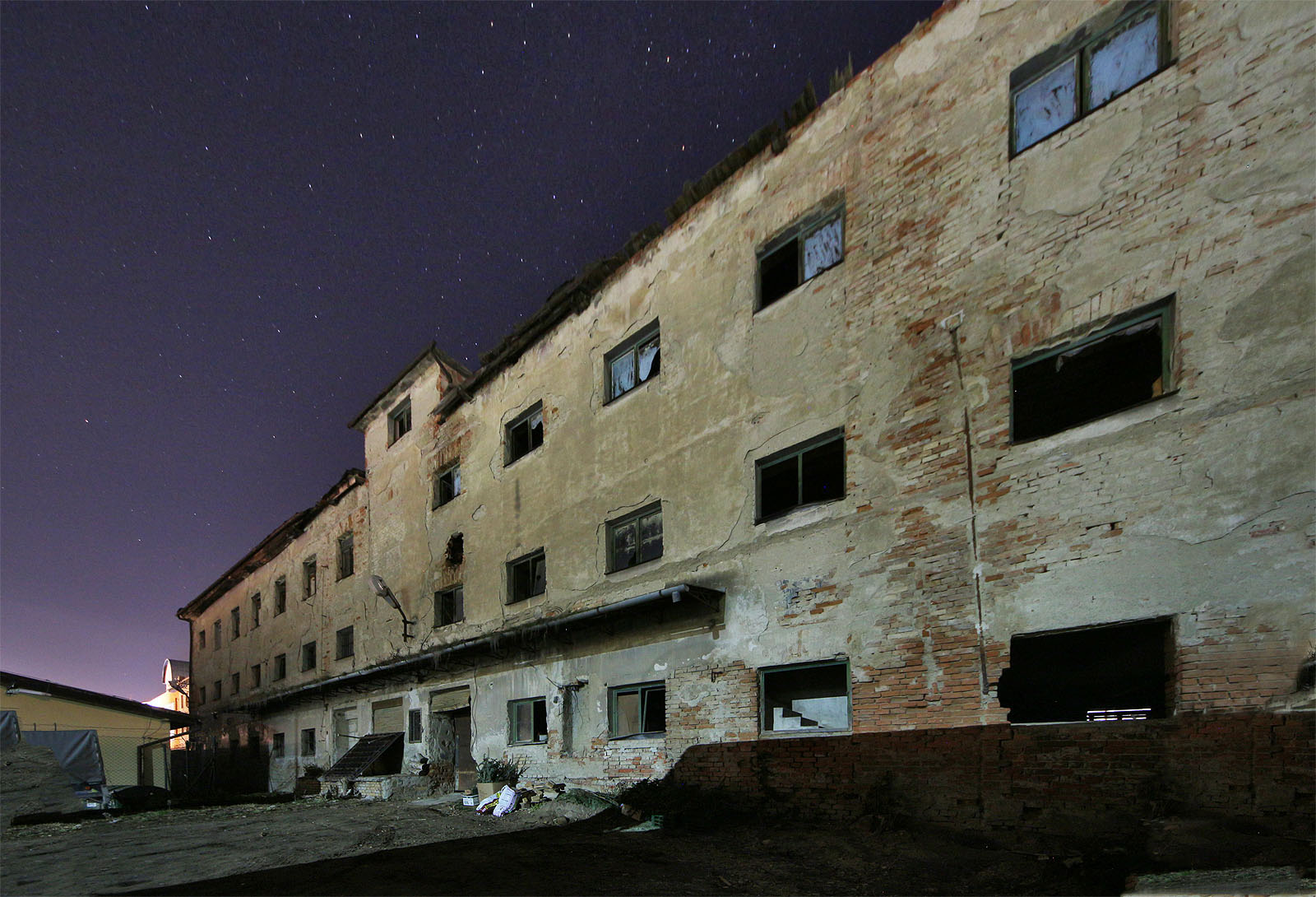 Na nočním snímku severovýchodní ze dvou budov Langovy tkalcovny je dobře vidět rozdíl mezi původními okny v jihozápadním a upravenými okny v severovýchodním křídle budovy. V pozadí je vidět druhá část tkalcovny, nasvětlená budova čp. 139.