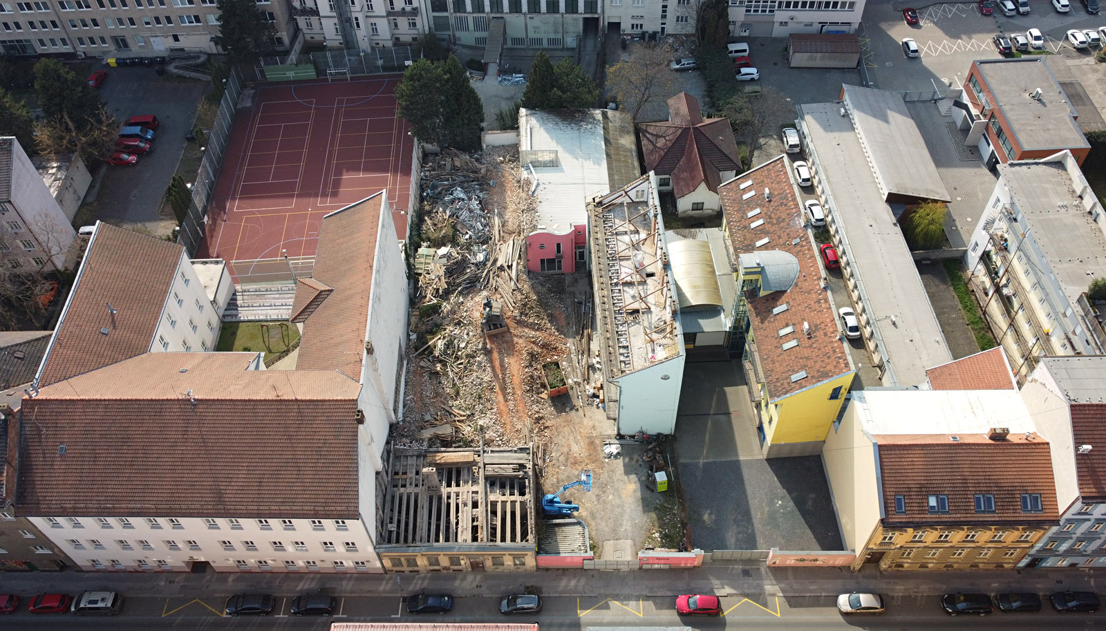 Pohled na demolované domy na adrese Příční 12 a Příční 14 Brno od východu. Vlevo na fotografii je vidět budova nižšího stupně gymnázia na tř. kpt. Jaroše (Příční 16), vpravo pavlačák Příční 10 a bytový dům příční 8. Místo dopadu americké bomby se nachází uprostřed snímku dole za růžovou zdí.