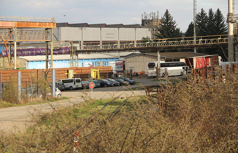 Vlečka Kovošrotu se proplétá mezi továrními a skladovými halami, potrubím a zaparkovanými auty zaměstnanců.
