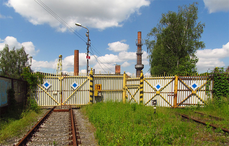 Tři koleje prochází přes plot areálu třemi branami (ta třetí je vlevo mimo fotku).